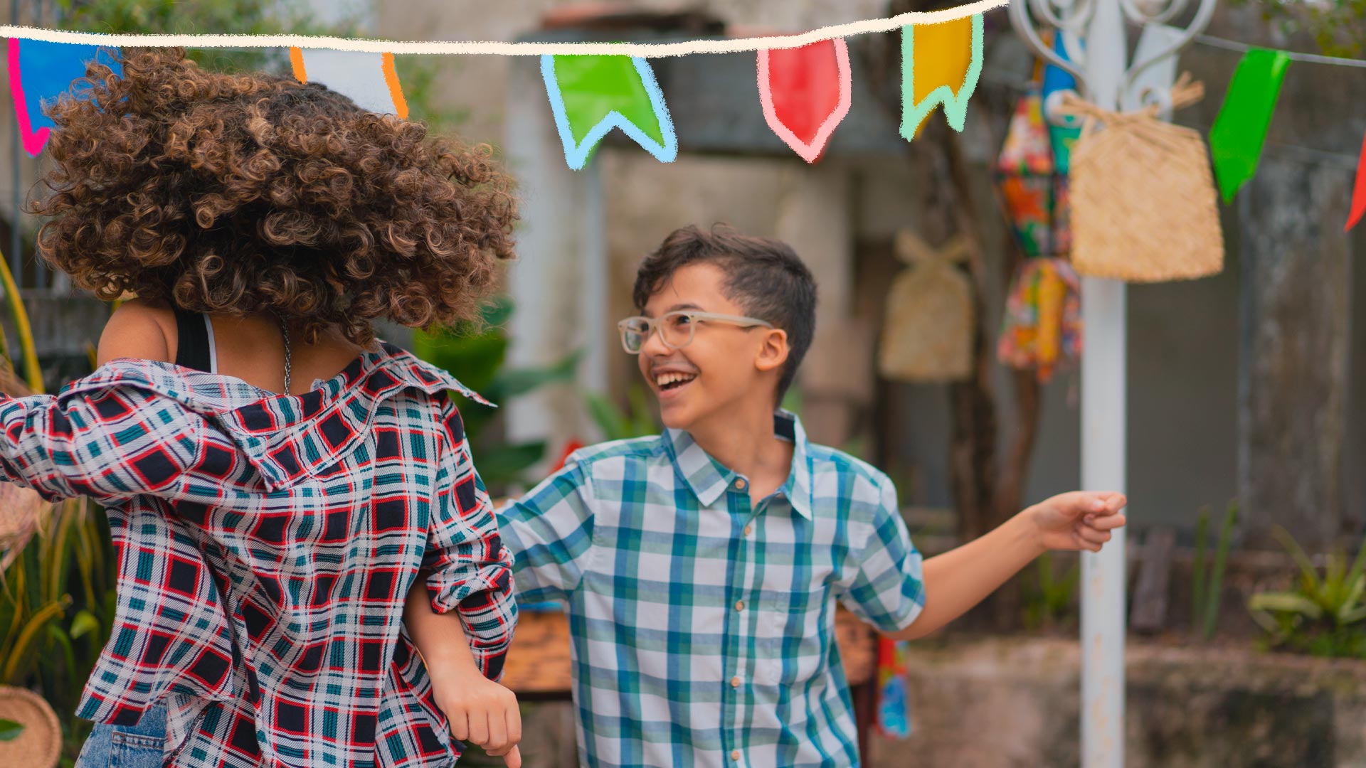 Crianças dançam em uma festa junina caseira, com bandeirolas decorando o ambiente.