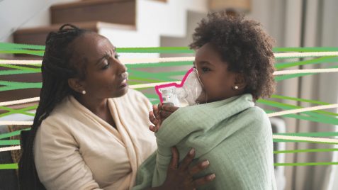 Na foto, uma mulher negra está ajudando uma criança negra, enrolada em uma pano, a respirar com um inalador.