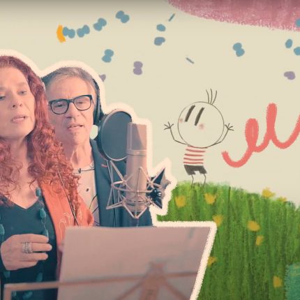 Na foto, Sandra Peres e Paulo Tahit na gravação da música Sementes. Os dois possuem pele clara e estão cantando na frente de um microfone.