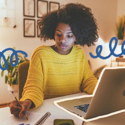 Uma mulher negra realiza anotações em um caderno, ao lado de um notebook.