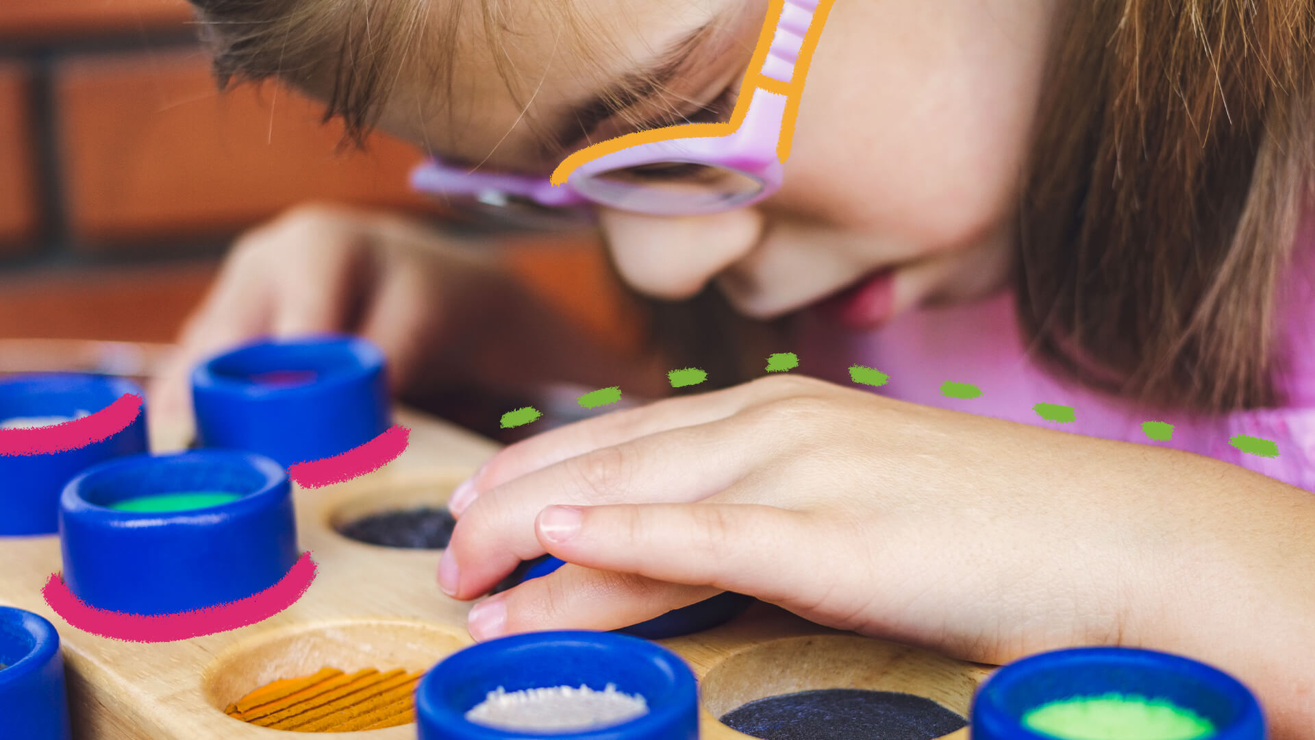 Atividades inclusivas: foto de uma criança de pele clara que brinca com pigmentos de diversas cores em uma superfície de madeira.