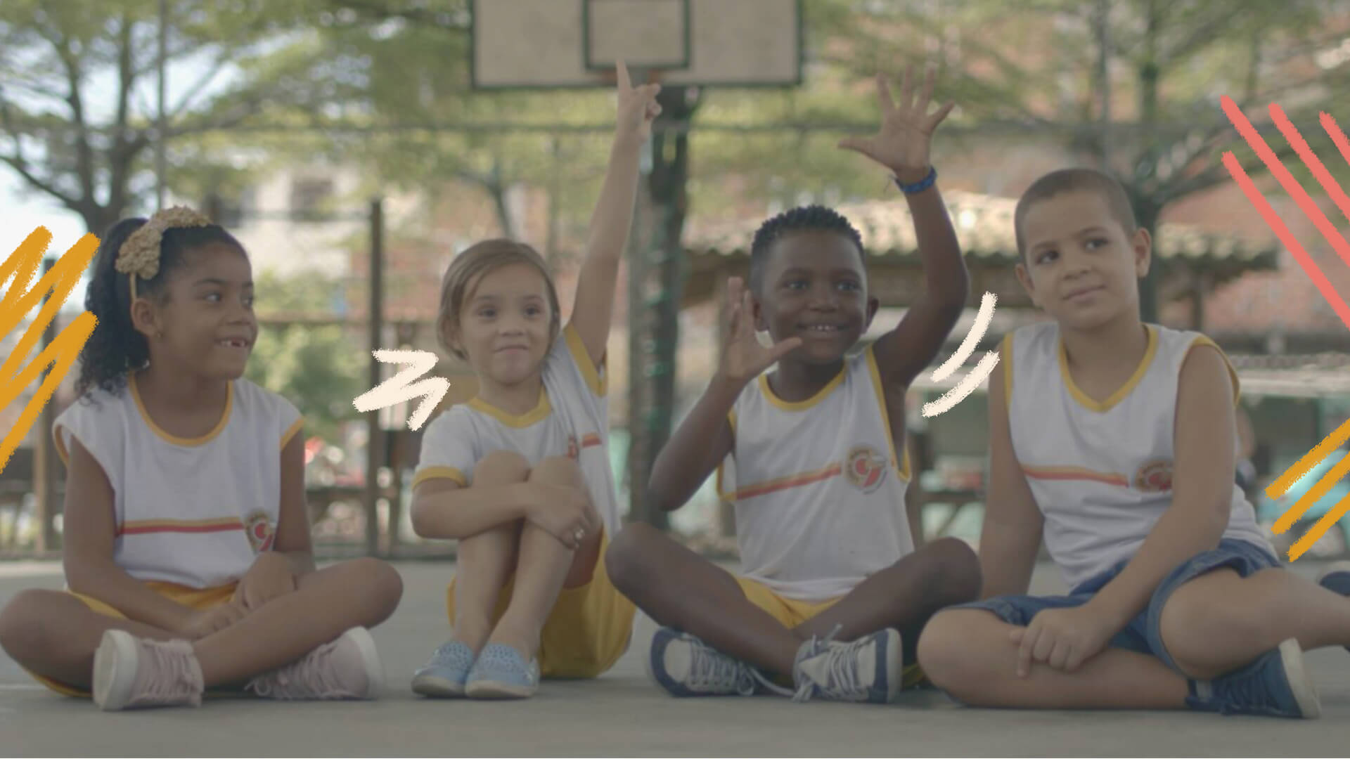 Imagem com um grupo multiétnico de crianças sentadas, que vestem um uniforme escolar branco.