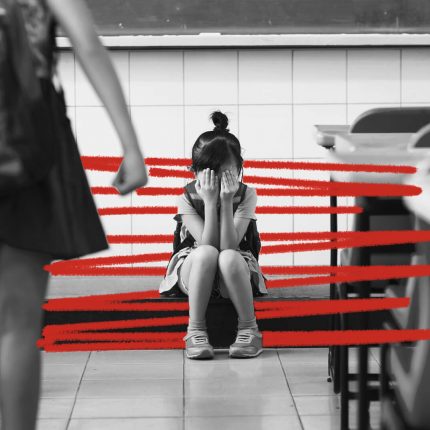 Uma menina está sentada no chão de uma sala de aula, escondendo o rosto com as mãos. A imagem está em preto e branco e possui rabiscos vermelhos.