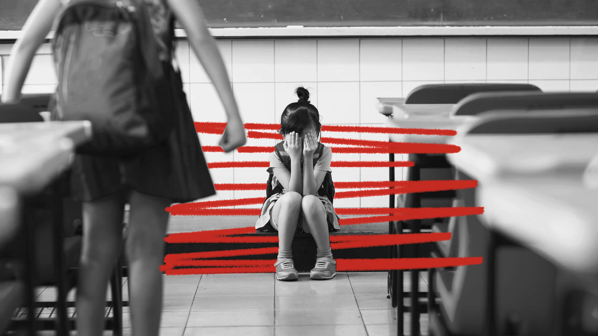 Uma menina está sentada no chão de uma sala de aula, escondendo o rosto com as mãos. A imagem está em preto e branco e possui rabiscos vermelhos.