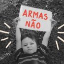 Foto em preto e branco de um menino segurando um papel escrito "Armas não"