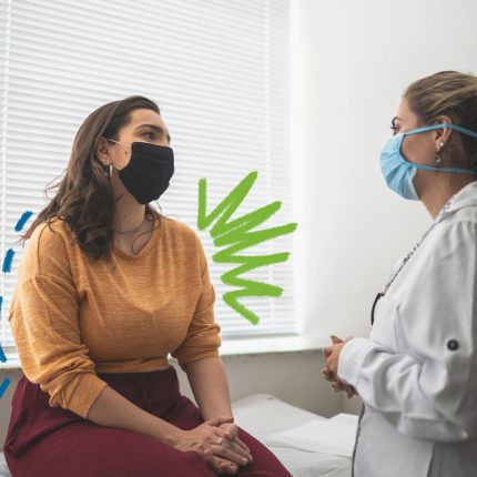 Duas mulheres brancas conversam em uma sala de consultório. Uma está sentada em uma maca, usa roupas em tons terrosos e uma máscara descartável preta. A outra utiliza um jaleco branco e utiliza uma máscara descartável azul.