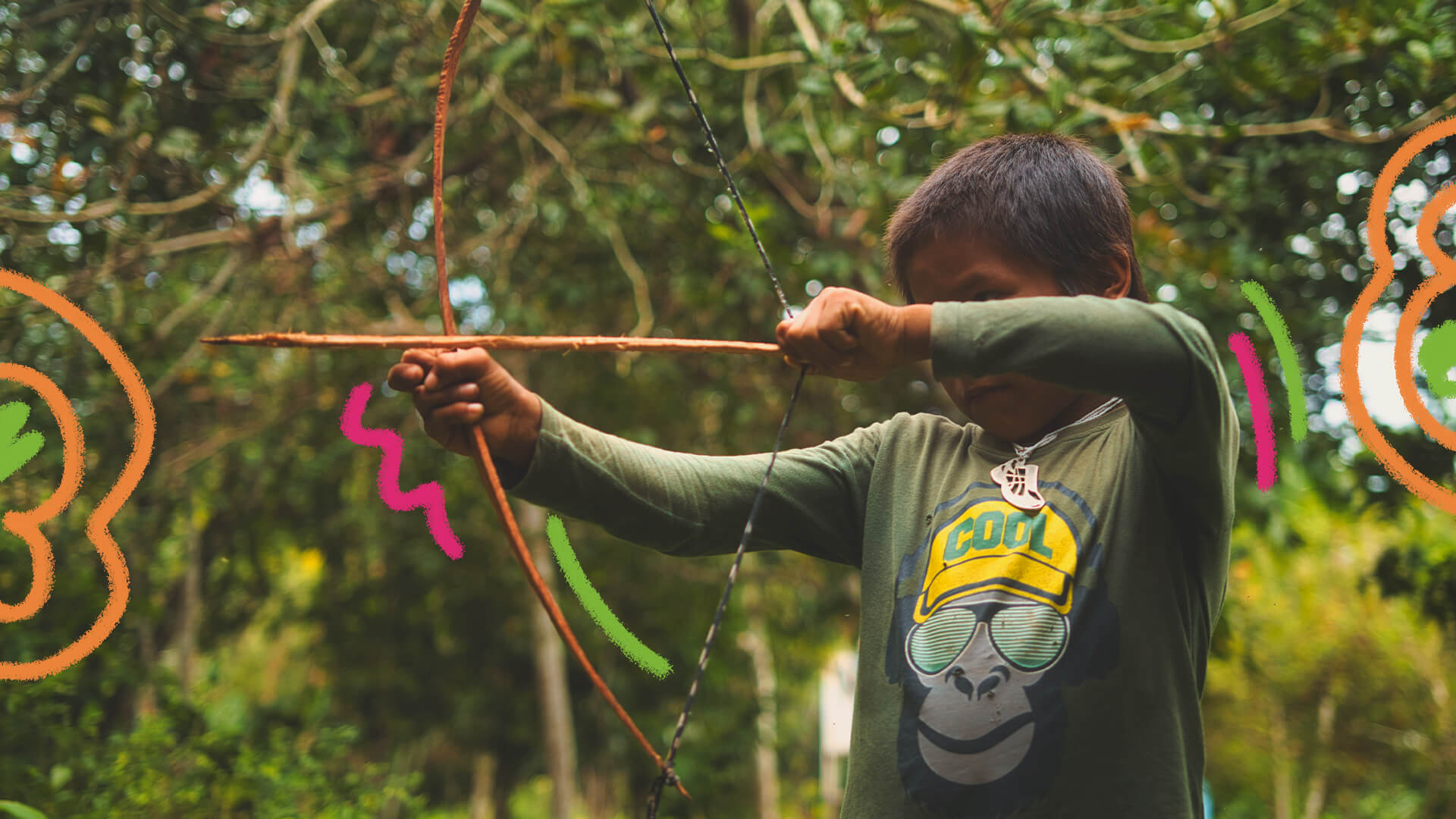 Um menino indígena empunha um arco e flecha em meio à natureza. Ele veste uma camiseta verde com a estampa de um macaco de óculos e boné amarelo. A matéria é sobre cultura no currículo e fortalecer o povo Huni Kuin