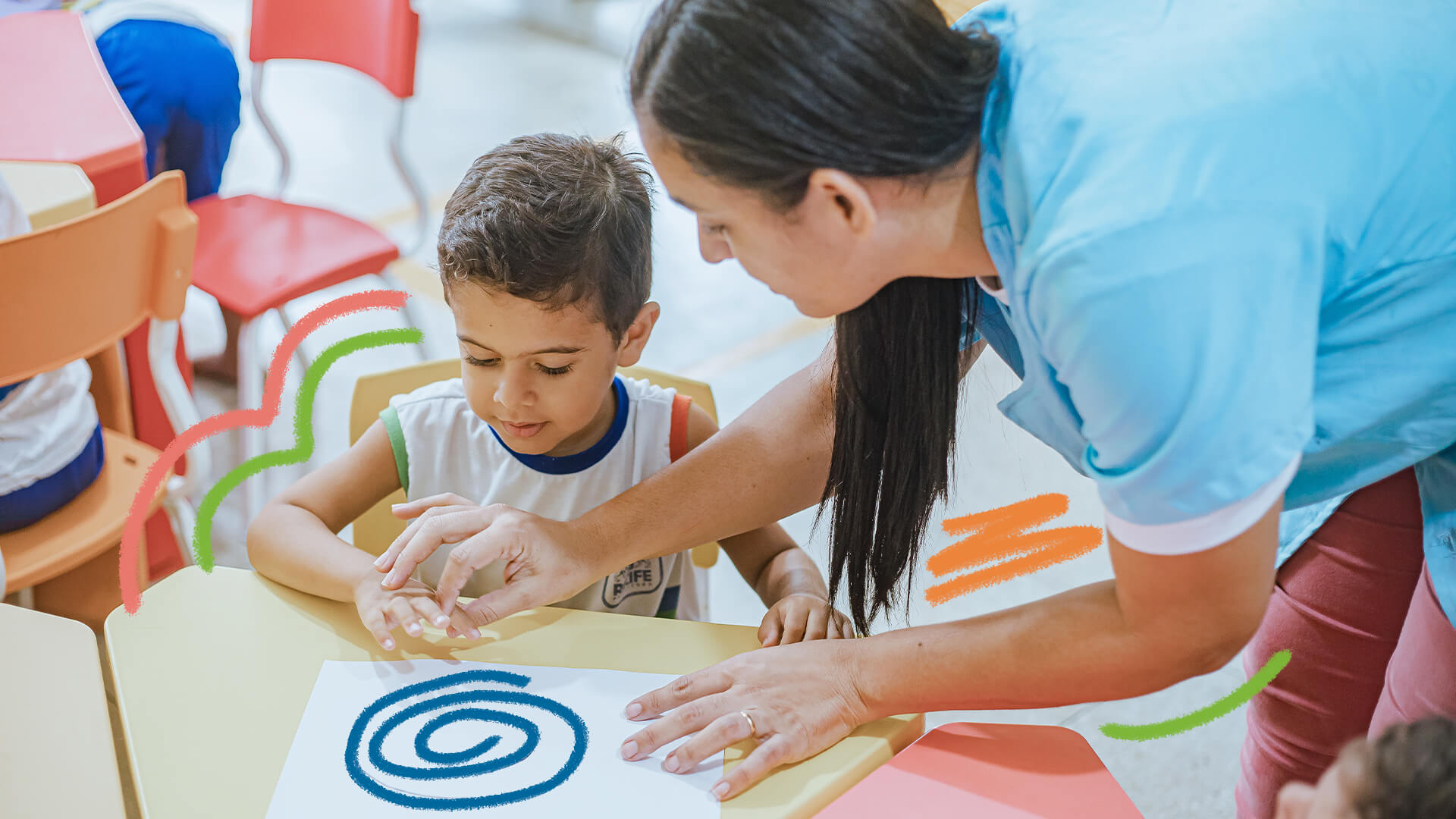 Educação infantil de qualidade:fiti de menino está sentado em frente a uma carteira sendo instruído por uma mulher (professora), desenhando um espiral num papel.