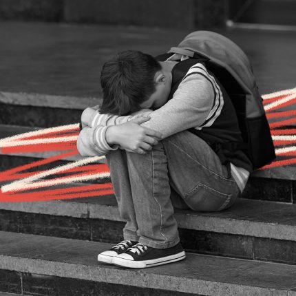 Foto em preto e branco de um menino, usando jeans e moletom e mochila nas costas, sentado em uma escadaria com o rosto escondido por entre os joelhos.