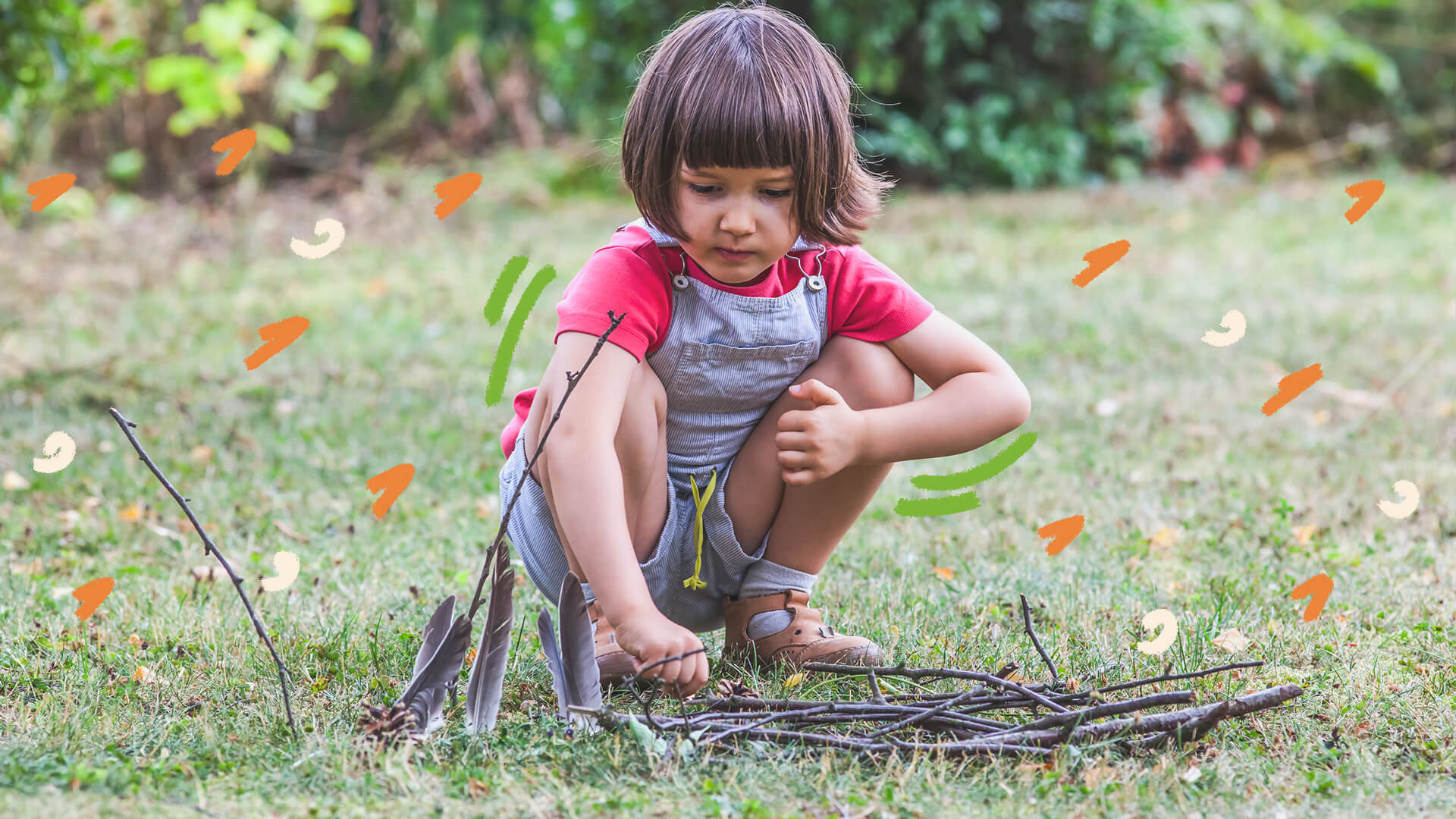 Brincar heurístico: foto de uUma menina de pele clara e cabelos castanhos curtos brinca com folhas e gravetos em um ambiente com grama e plantas. Ela veste um macacão azul com camisa rosa.