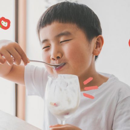 Morangos com iogurte: Um menino de etnia amarela sorri enquanto come uma sobremesa em uma taça de vidro.