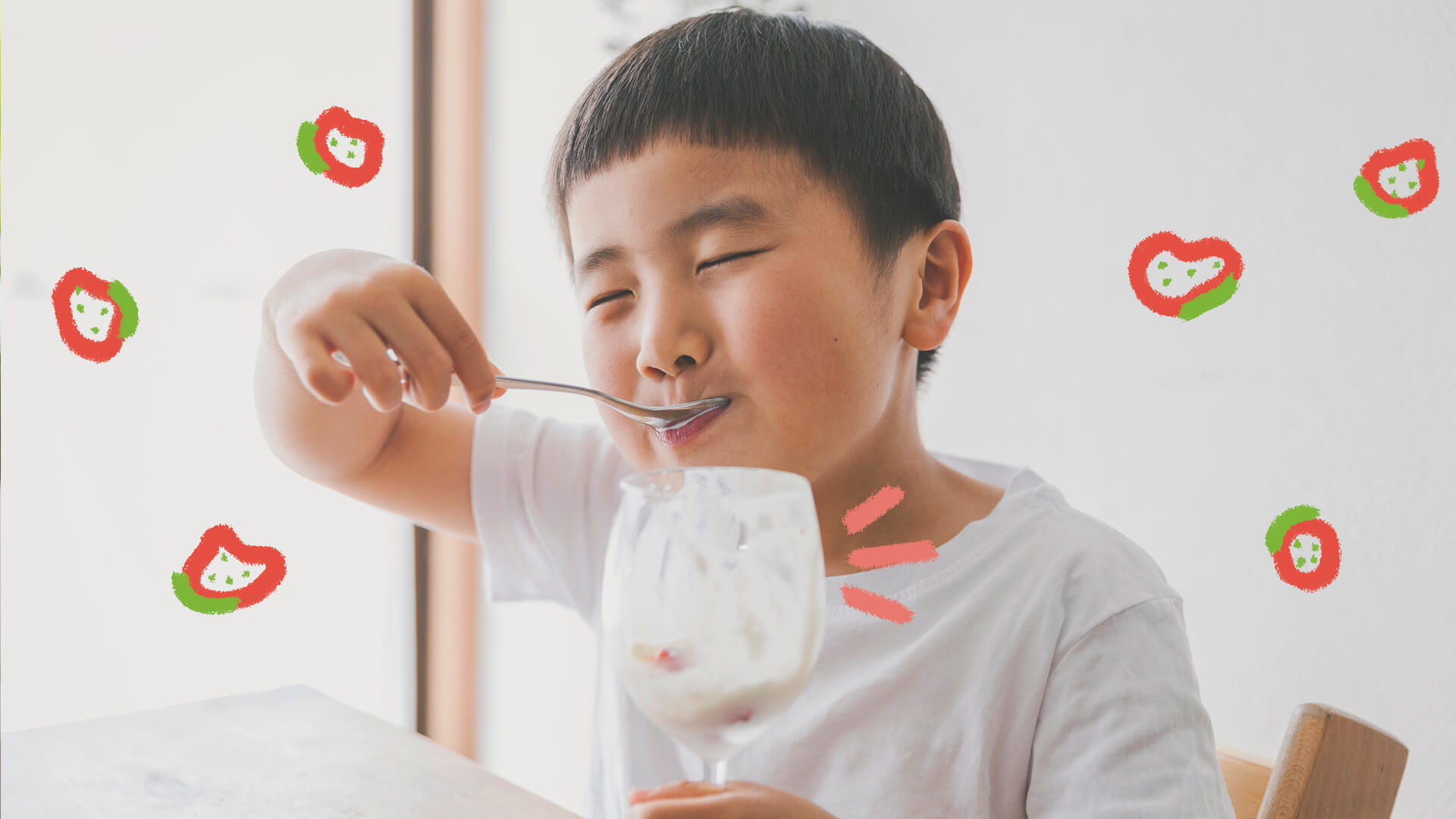 Morangos com iogurte: Um menino de etnia amarela sorri enquanto come uma sobremesa em uma taça de vidro.