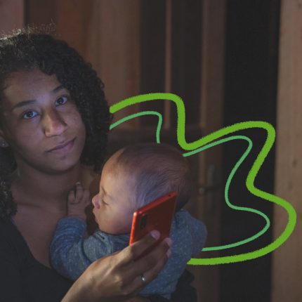 A imagem mostra uma adolescente negra, de cabelos cacheados, com um bebê recém-nascido no colo e um celular nas mãos.