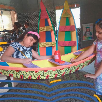 Foto de duas crianças pintando uma embarcação feita de miriti
