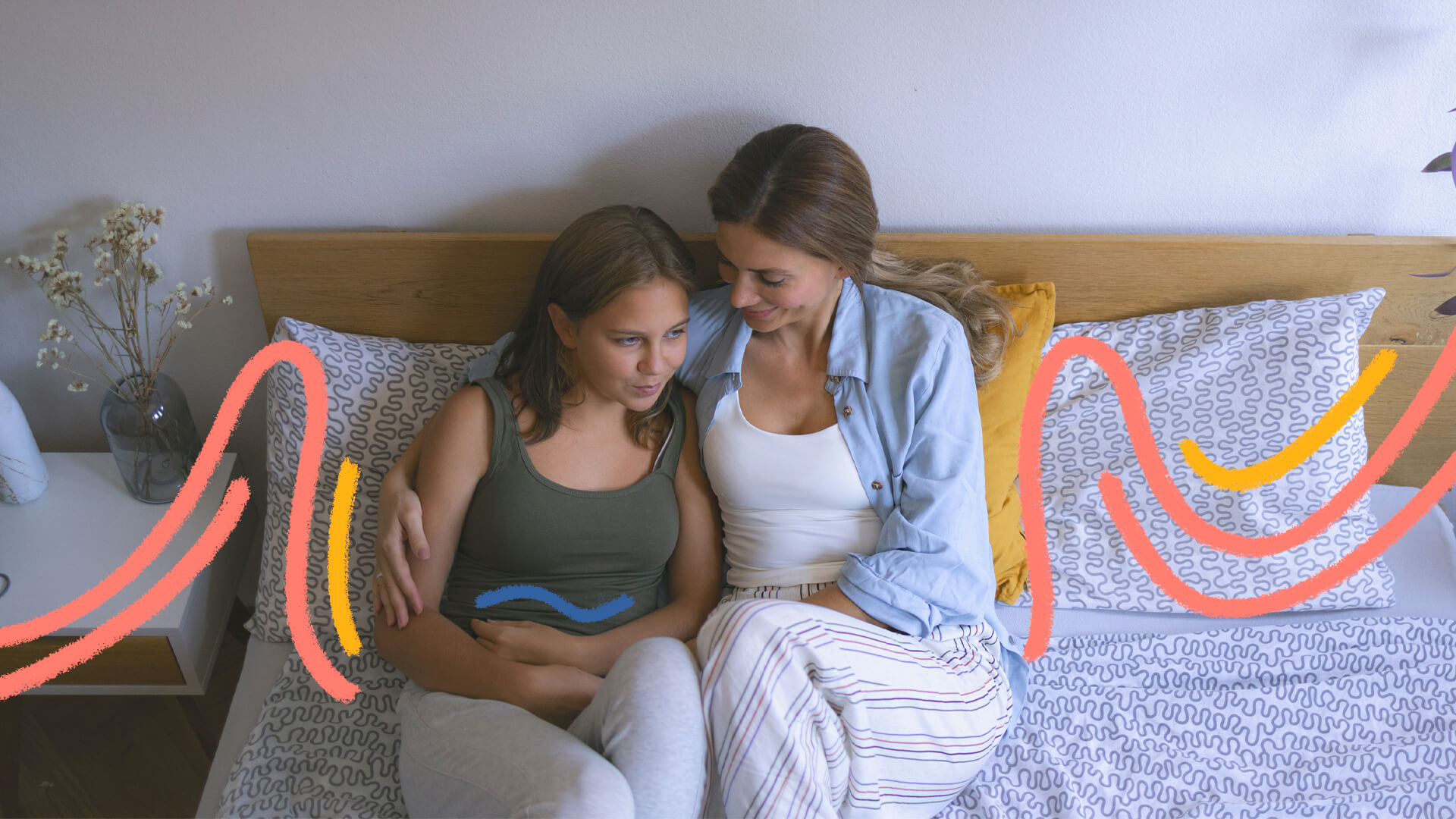 Mãe e filha adolescente estão sentadas conversando. A garota está com os braços cercando a região da barriga. A imagem ilustra uma matéria sobre primeira menstruação.