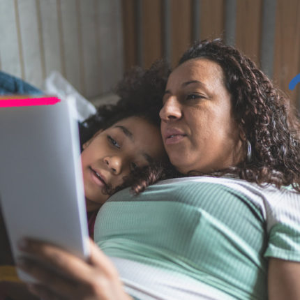 Foto de uma mulher e uma menina que estão deitadas lendo o mesmo livro juntas