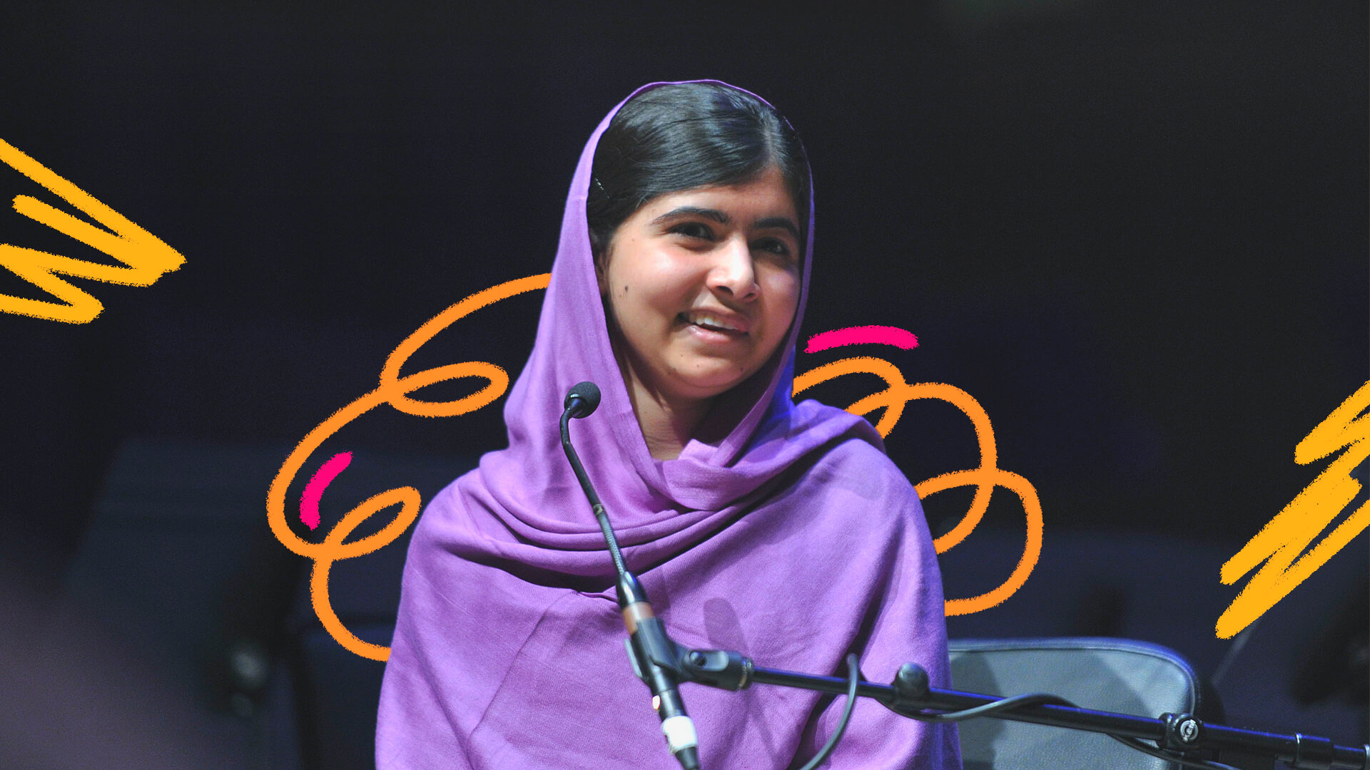 Foto da ativista paquistanesa Malala Yousafzai em matéria que apresenta 3 livros às crianças sobre sua luta para que todas as meninas estudem e em comemoração ao Dia de Malala. Ela está diante de um microfone, tem cabelos pretos e veste roxo.