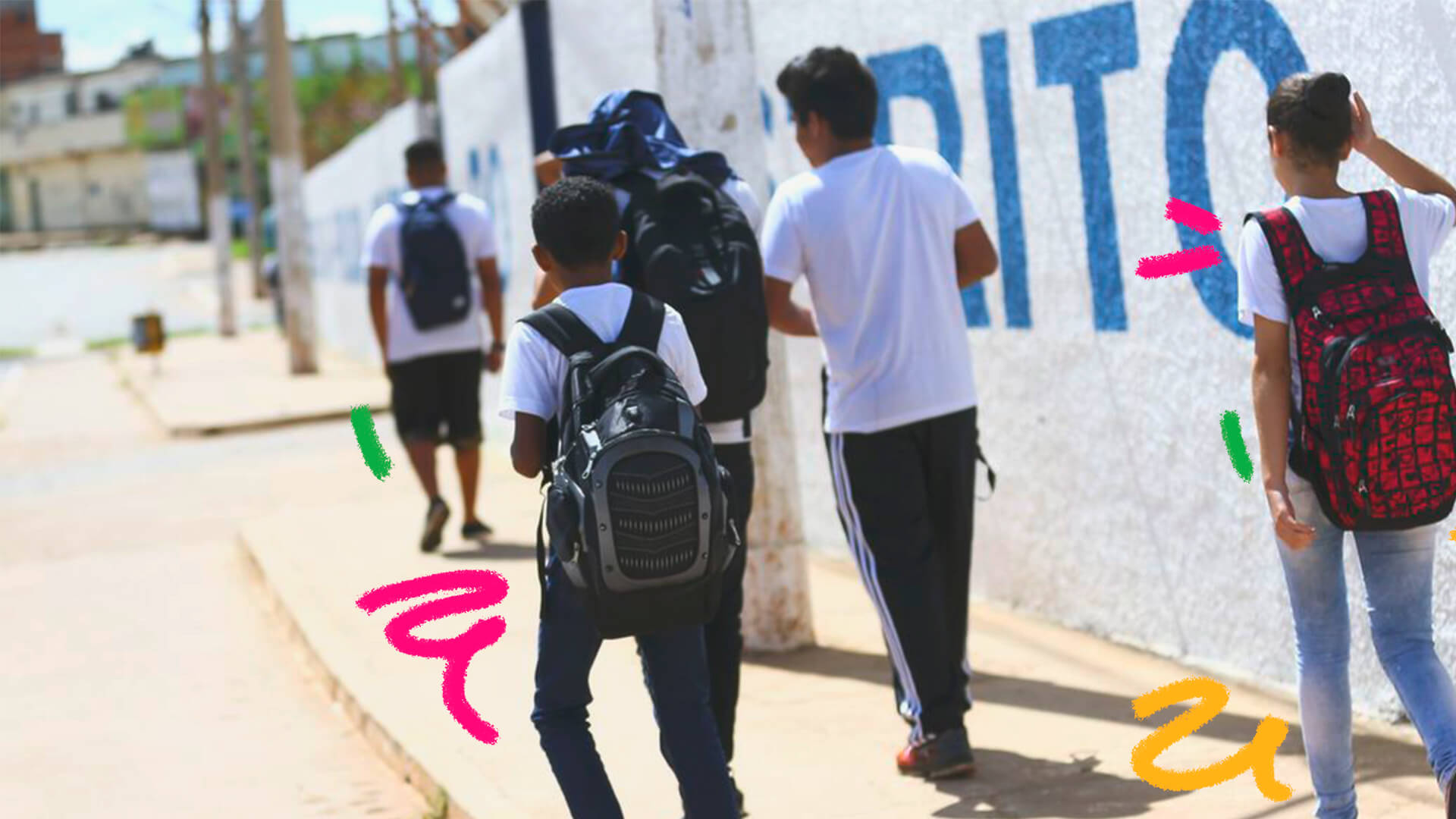 Um grupo de quatro jovens caminham por uma calçada, em paralelo a um muro. Eles usam uniforme escolar e três deles carregam mochilas nas costas