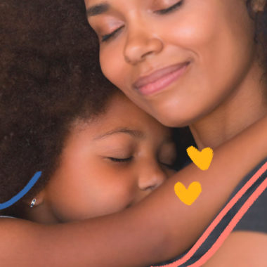 Mulher e criança se abraçam. Ambas são negras e de cabelos cacheados. A matéria trata de alisar o cabelo na infância.