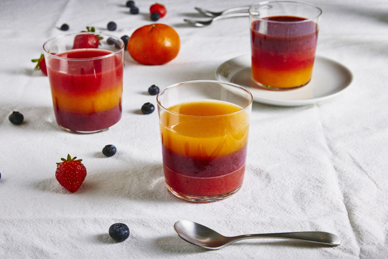 receita de gelatina de frutas: a sobremesa está em três copos disposto na mesa. A gelatina tem três cores: vermelho, laranja e roxa.