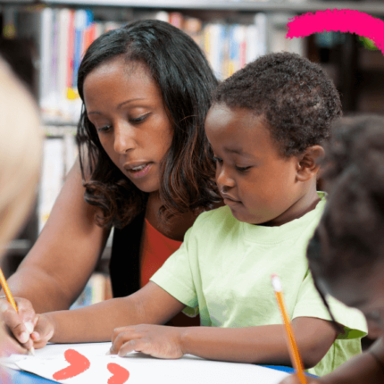 Imagem para matéria sobre educação antirracista mostra uma professora negra sentada aolado de dois alunos, um menino e uam menina negros, que escrevem com lápis em um papel.