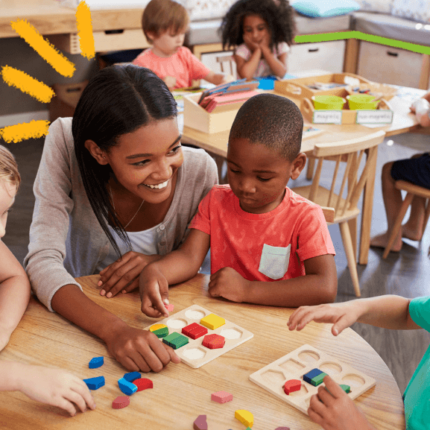 imagem ilustra matéria de hierarquia racial entre as crianças mostra uma professora negra agachada entre três crianças em uma sala de aula.