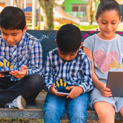 Imagem ilustra matéria sobre o uso do youtube por crianças. Dois meninos e uma menina estão sentados em um banco de praça utilizando telas de smatphones e tablets.