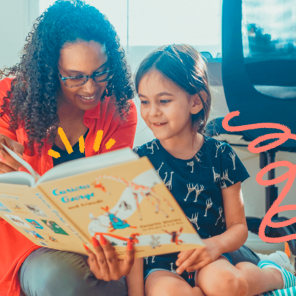 imagem ilustra matéria sobre hábitos de leitura entre as crianças e mostra uma mulher negra, de cabelos cacheados e óculos, sentada ao lado de uma menina branca, de cabelos lisos, que segura um livro na mão.