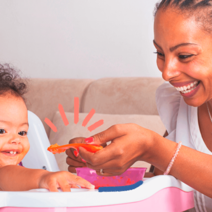 imagem ilustra matéria sobre o guia alimentar da OMS e mostra um bebê negro sentado em uma cadeirinha de alimentação, srrindo e comendo ao lado d amãe, uma mulher negra, sorrindo e segurando um prato de comida.