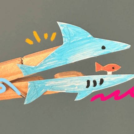 imagem mostra um desenho de um tubarão feito de papel colado em um pregador de roupa de madeira