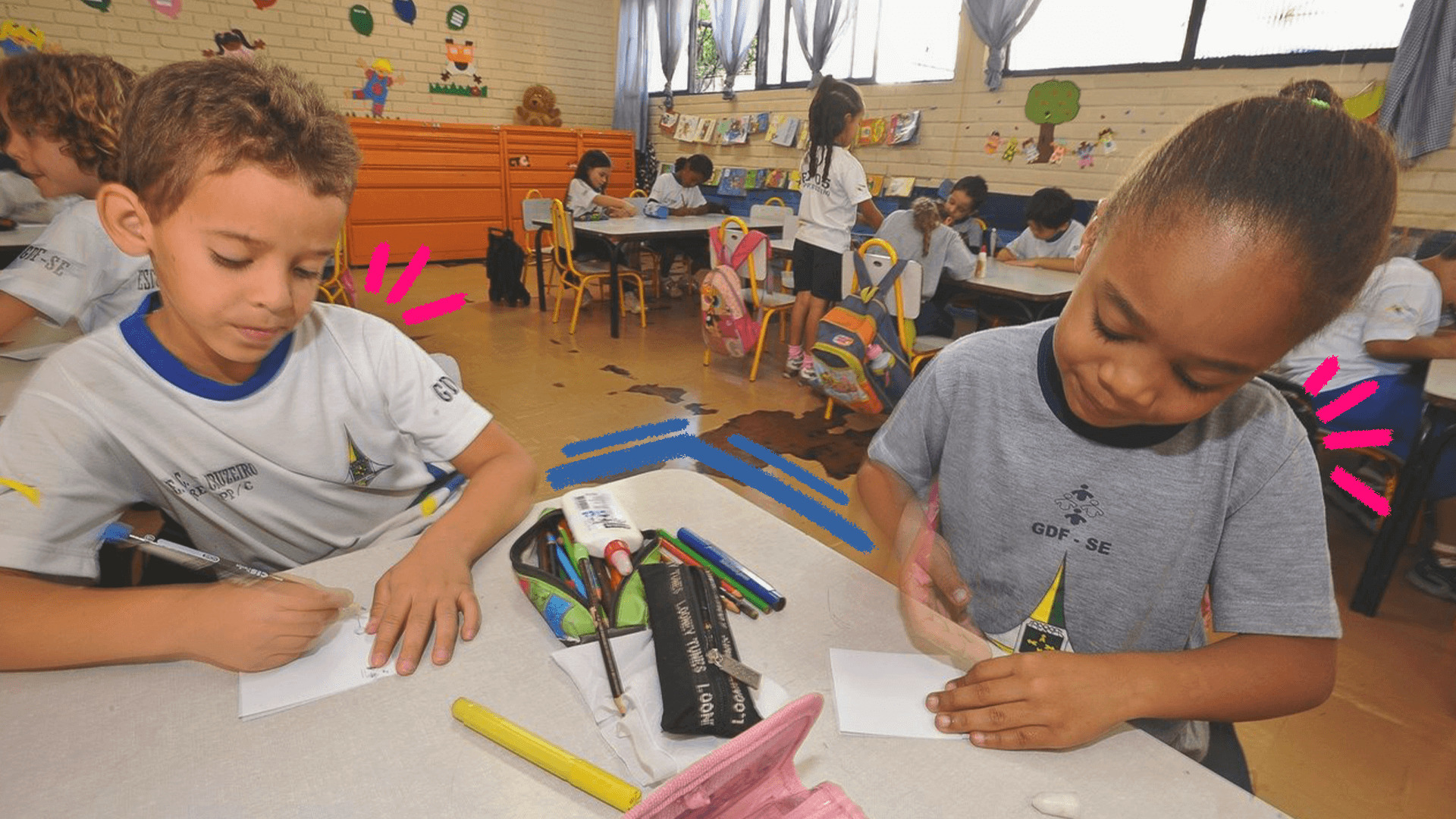 Imagem ilustra a matéria sobre a pesquisa educação infantil mostra uma sala de aula e duas crianças negras com uniforme, sentadas fazendo uma tarefa com lápis e papel.