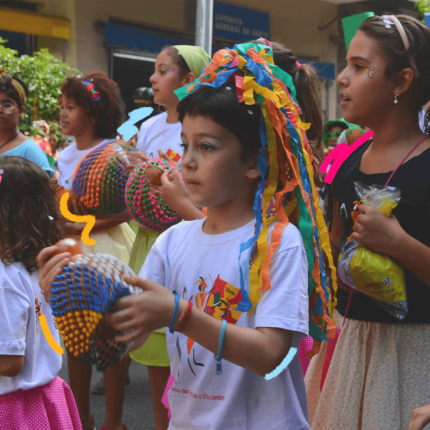 Imagem mostra crianças enfeitadas com adereços de carnaval brincando na rua. Foto ilustra a matéria sobre as regras d ecarnaval para crianças.