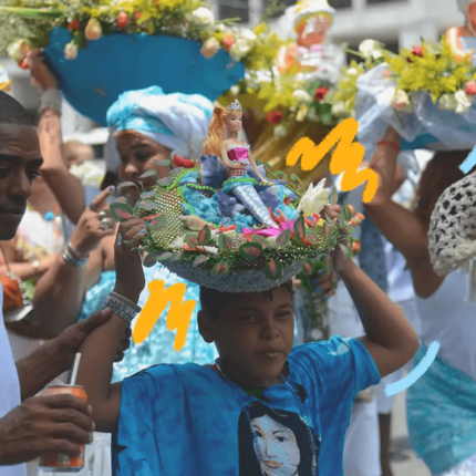 Imagem mostra uma criança celebrando iemanjá, com uma oferenda na cabeça, um cesto com uma imagem de iemanjá