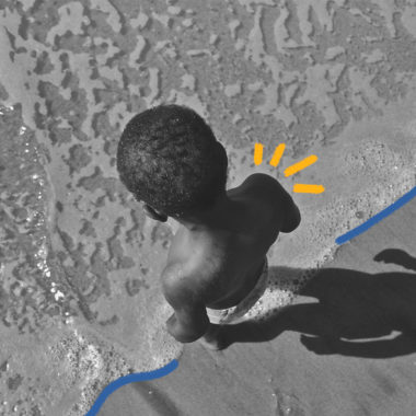 imagem em preto e branco ilustra matéria sobre a operação verão, no rio de janeiro e mostra um menino negro vito de cima, na beira de uma praia.