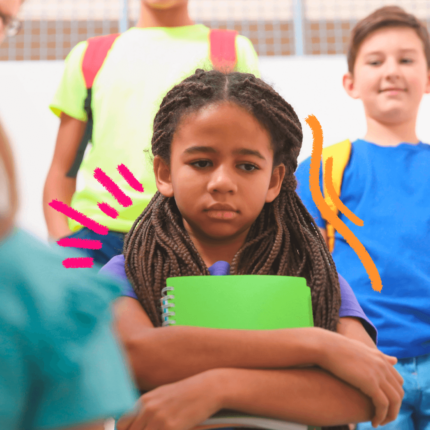 Uma menina negra de tranças segurando um caderno verde olha para o chão em meio a colegas na escola