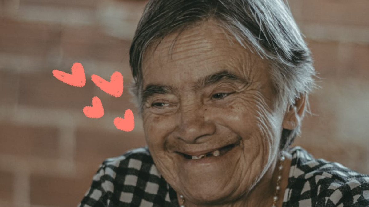 Foto de Izabel, uma idosa de 70 anos que descobriu a síndrome de Down aos 35. Ela usa blusa quadriculada de preto e branco com uma flor vermelha e colar de pérolas