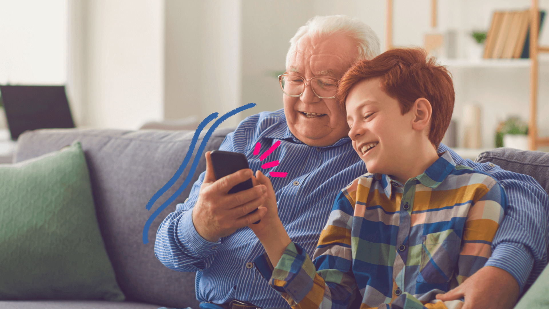 Um homem idoso de cabelos brancos e camisa azul divide com um menino ruivo de camiseta listrada a tela de um celular. Os dois estão sentados num sofá cinza. A matéria fala sobre a resolução do Conanda e a proteção de crianças no ambiente digital.