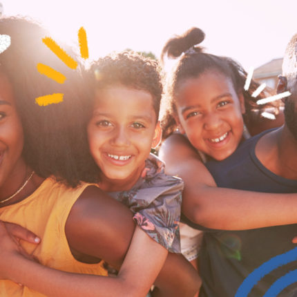 Imagem de uma familia de pessoas negras com dois filhos, um menino e uma menina. Todos usam roupas coloridas e estão se abraçando e sorrindo. A matéria é sobre a lei de parentalidade positiva e direito ao brincar.