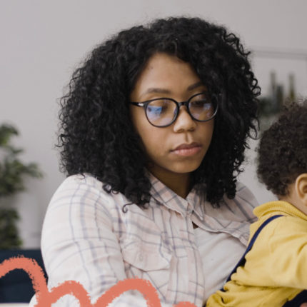 imagem de capa de matéria sobre sobrecarga materna mostra uma mulher negra de cabelos cacheados usando o computador e segurando no colo uma criança.