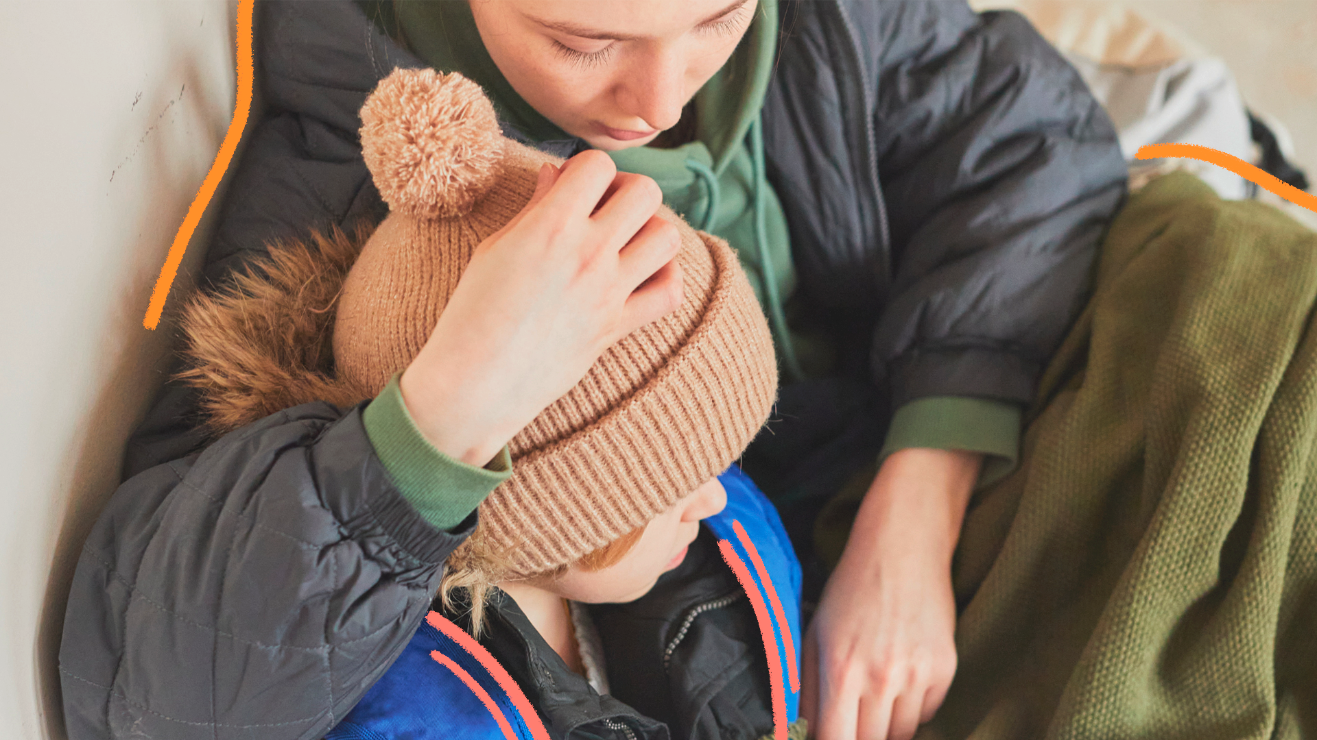 imagem de capa para matéria sobre como proteger as crianças nos abrigos do RS mostra uma mulher ventindo roupas de frio abraçando uma criança, menino branco com touca de frio. Ambos estão sentados.