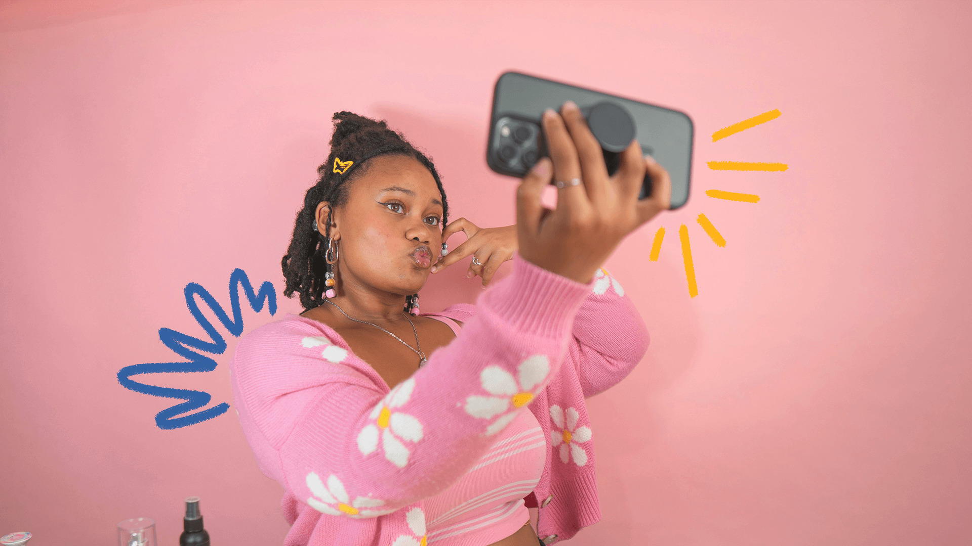 Foto de uma adolescente negra vestindo moletom rosa com estampa de flores brancas segurando o celular e fazendo pose para uma selfie. O texto fala sobre como os adolescentes veem como espelho os algoritmos das redes sociais.