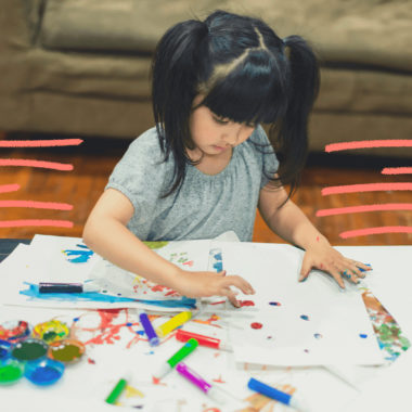 Imagem de capa sobre tipos de pinturas para fazer em casa mostra uma menina branca com traços orientais sentada, pintando com canetas coloridas em um papael branco.