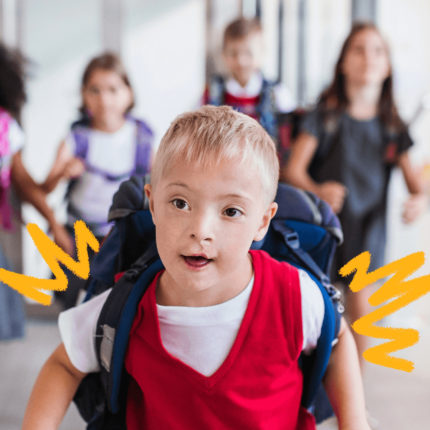 imagem de capa para matéria sobre a evolução da educação especial mostra um menino branco com síndrome de down, usando uniforme escolar e mochila, correndo em um pátio de escola com outras crianças ao fundo