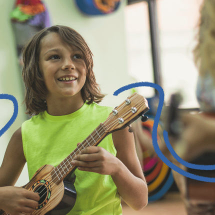 imagem de capa para matéria sobre criatividade crianças mostra um menino branco, de cabelos longos segurando um ukulelê em uma aula de música