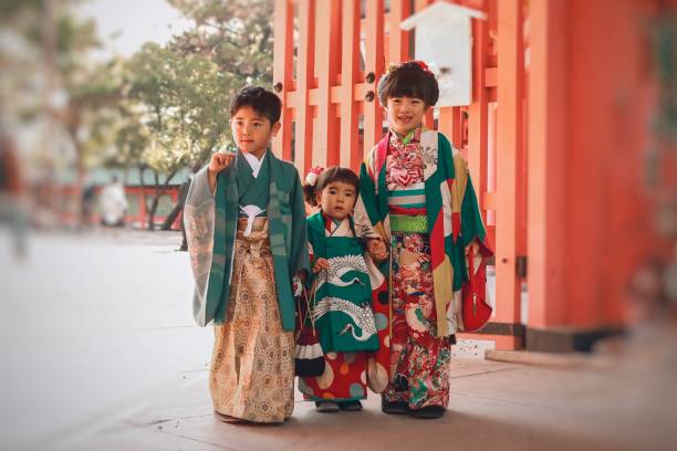 Imagem mostra três crianças japonesas vestindo kimonos verde e vermelho. 