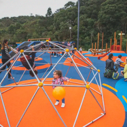 Imagem de capa para matéria sobre parques inclusivos mostra um parque colorido com binquedos inclusivos e crianças brincando.