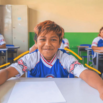 Imagem de capa para matéria sobre línguas indígenas mostra uma sala de aula em uma escola indígena. Em destaque, um estudante menino, pardo, com traços indígenas e cabelos curtos e uniforme escolar.