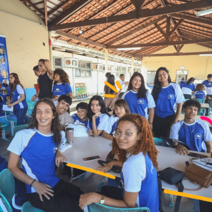 Foto de um grupo de adolescentes reunidos em volta de uma mesa. Todos usam uniforme azul e branco.