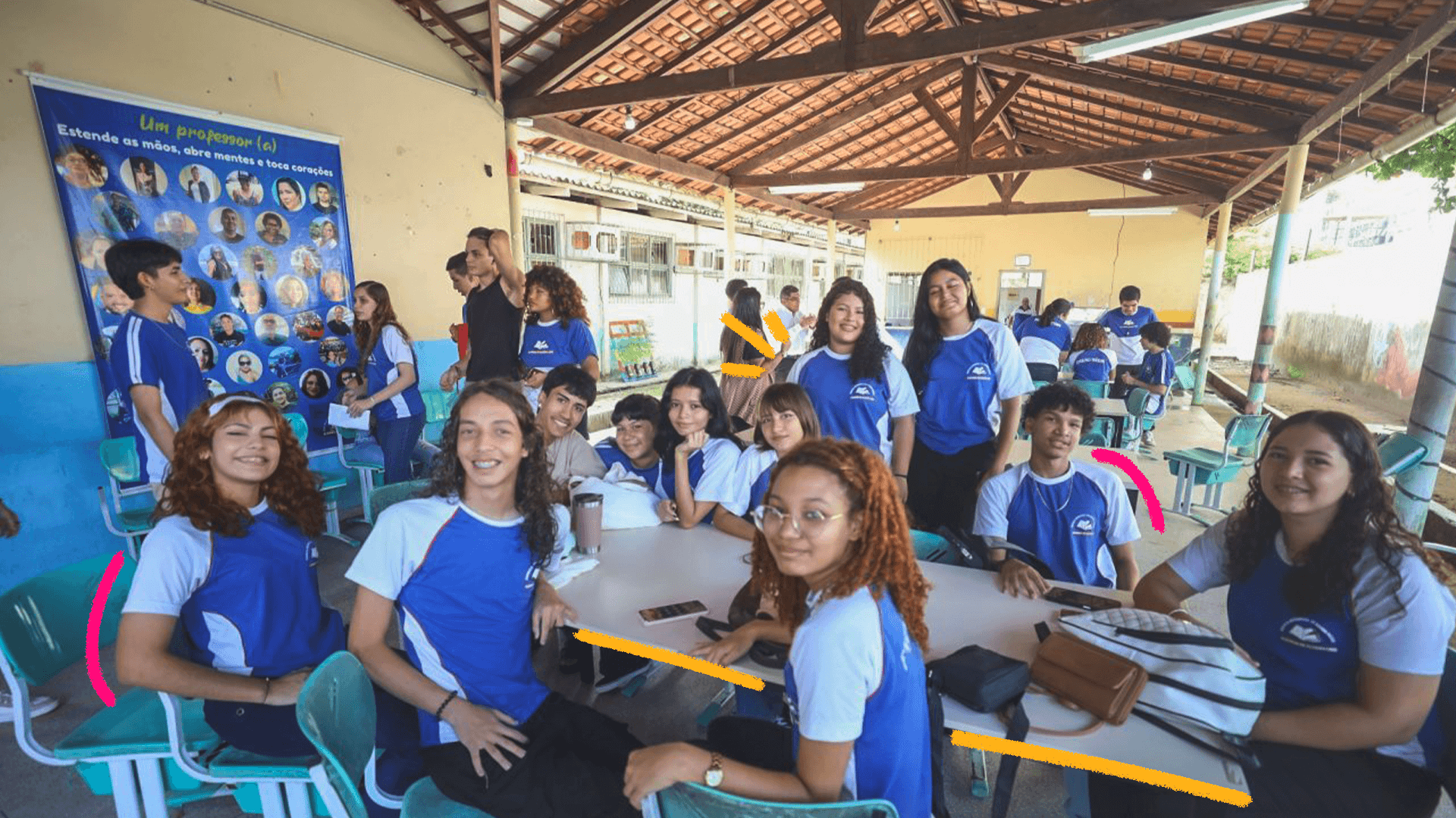 Foto de um grupo de adolescentes reunidos em volta de uma mesa. Todos usam uniforme azul e branco.