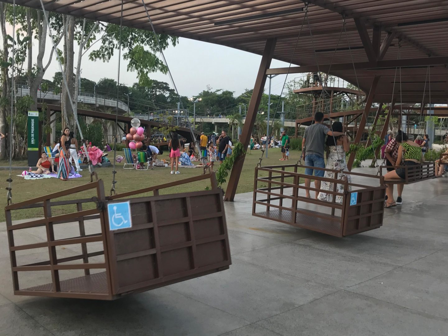 Imagem de parquinhoa inclusivos mostra o espaço do Parque Maguary, com área de balanço de madeira para cadeirantes. 